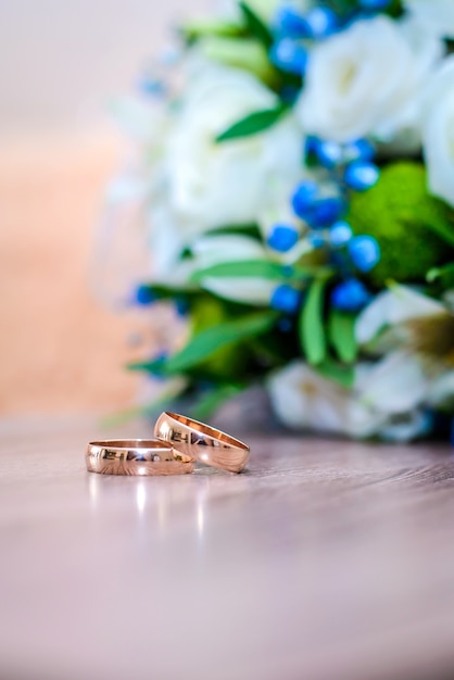 Bellissime fedi nuziali d'oro sul tavolo accanto al bouquet della sposa di fiori bianchi e blu