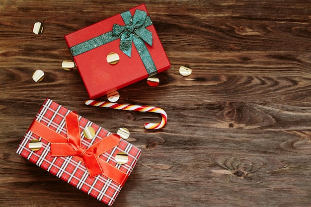 Bellissime palline rosse di Natale e un regalo rosso con un nastro verde con lecca-lecca su uno sfondo di legno Concetto di natale di capodanno Mockup festivo piatto con spazio di copia