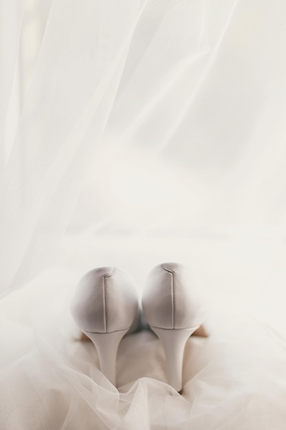Bellissime scarpe eleganti su abito da sposa in seta di lusso semplici scarpe bianche su abito bianco con ornamenti floreali in pizzo preparazioni mattutine nuziali
