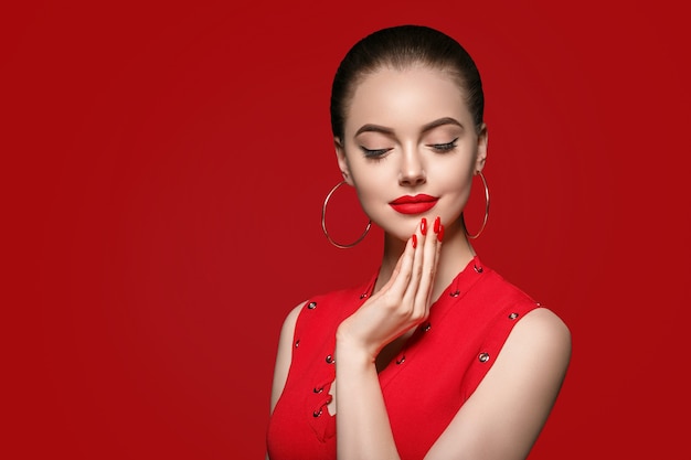 Bellissimi capelli ricci femminili in rosso con labbra rosse e manicure vestita, acconciatura afro rosa di bellezza su sfondo rosso. Colpo dello studio.