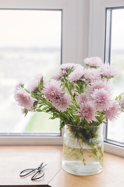 Bellissimi fiori autunnali e forbici alla luce sul davanzale in legno Astri rosa Accogliente casa in autunno