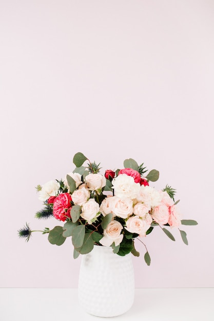 Bellissimi fiori bouquet rose magniloquenti, eringium blu, rami di eucalipto in vaso di fiori a parete rosa pink