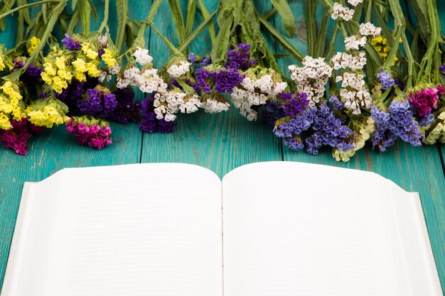 Bellissimi fiori colorati e libro bianco aperto su un tavolo di legno blu