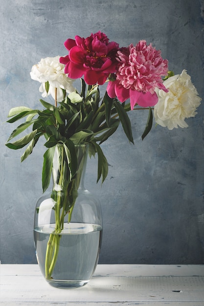 Bellissimi fiori di peonia bianca, viola e rosa in un vaso di vetro.