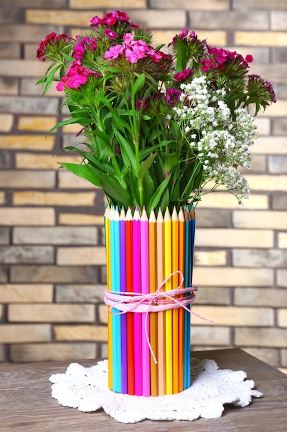 Bellissimi fiori in vaso di matite colorate sul fondo del muro di mattoni