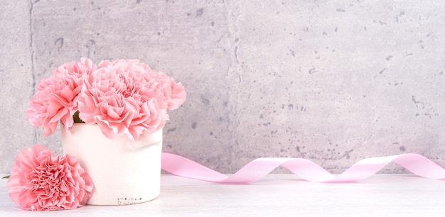 Bellissimi garofani in fiore con scatola di nastro rosa isolato su sfondo grigio chiaro, vicino, copia dello spazio