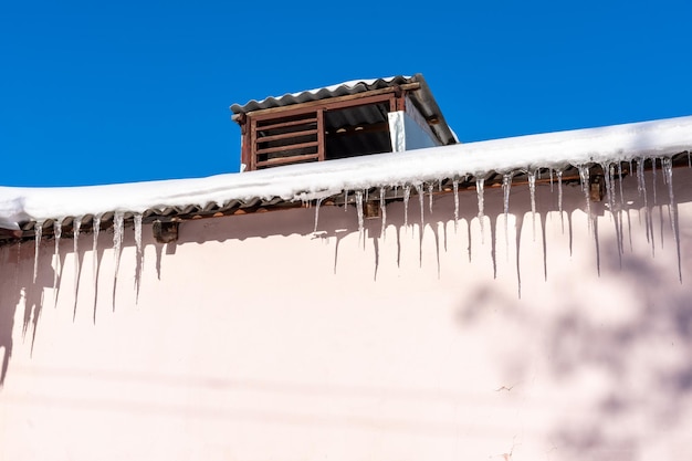 Bellissimi ghiaccioli appesi al tetto di una vecchia casa Lunghi ghiaccioli trasparenti pendono dal tetto innevato