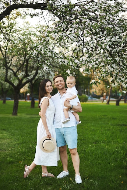 Bellissimi giovani genitori e il loro adorabile figlioletto si divertono vicino agli alberi in fiore, famiglia felice