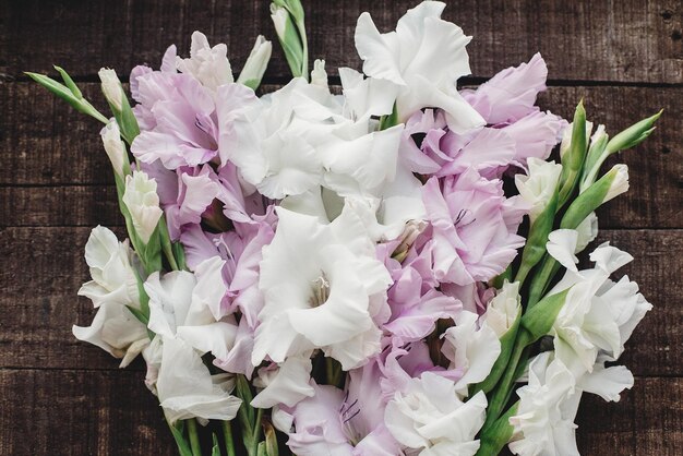 Bellissimi gladioli rosa e bianchi su fondo di legno rustico piatto laici gladioli colorati su spazio di legno marrone rustico per testo vacanza biglietto di auguri floreale immagine di primavera