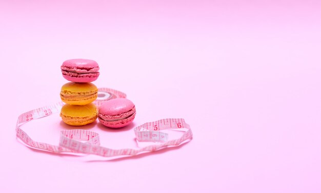 Bellissimi macarons rosa e gialli su sfondo rosa e nastro per misurare il volume del corpo. Dimagrimento di concetto