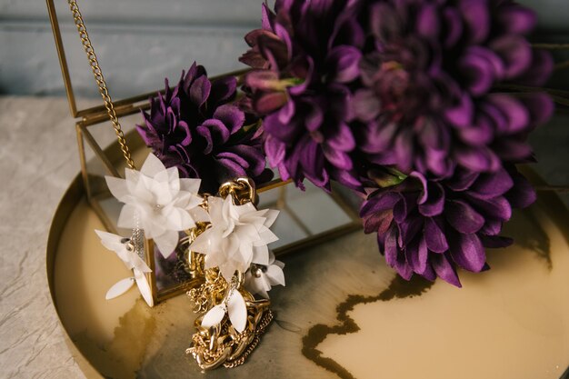 Bellissimi orecchini dorati accanto a fiori Dettagli interni di una camera da letto femminile