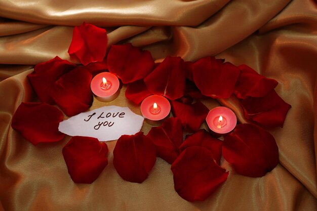 Bellissimi petali di rose rosse con candele e biglietto di auguri, primi piani