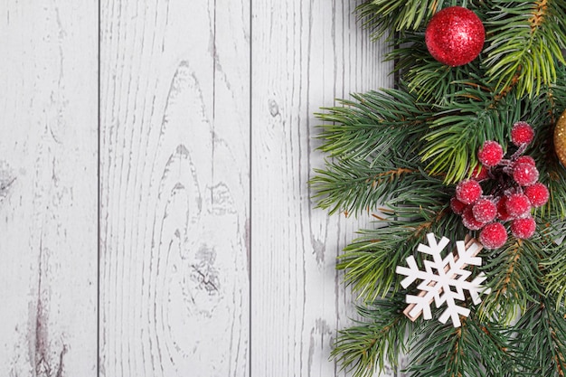 Bellissimi rami di un albero di Natale con coni e giocattoli su un fondo di legno bianco con la scritta Buon Natale