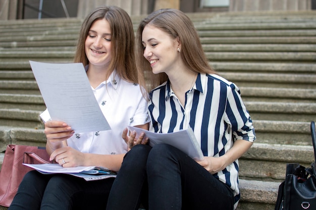 Bellissimi studenti seduti sui gradini vicino alla scuola