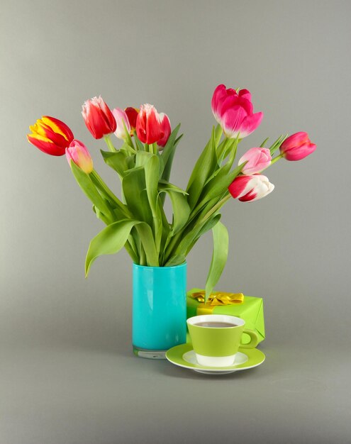 Bellissimi tulipani nel secchio con regali e tazza di tè su sfondo grigio