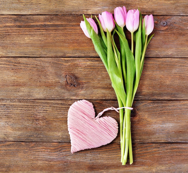 Bellissimi tulipani rosa con cuore decorativo su fondo in legno