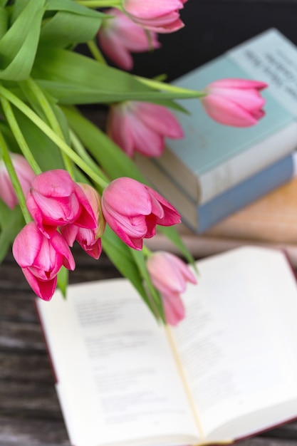 Bellissimi tulipani rosa in un vaso e libri sullo sfondo di un muro di mattoni
