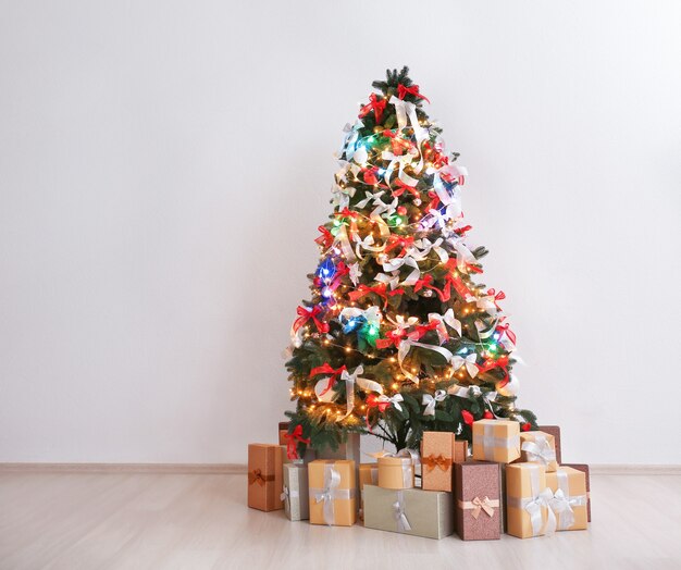 Bellissimo abete decorato per il Natale in una stanza vuota contro il muro chiaro