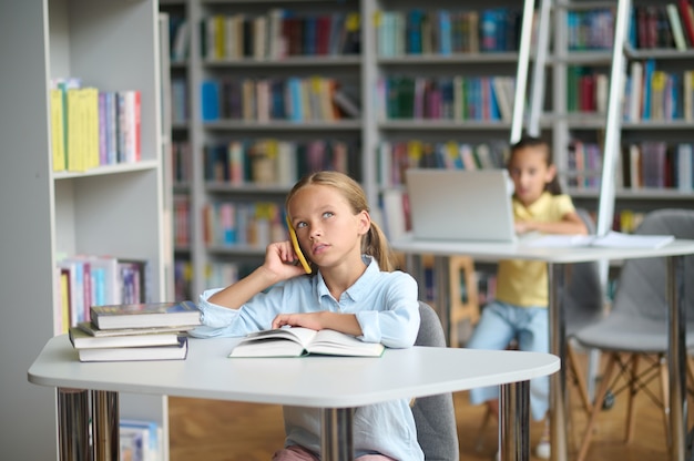 Bellissimo allievo che fa una telefonata da una biblioteca