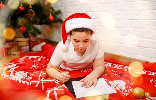 Bellissimo bambino che scrive la lettera santa vicino all'albero di natale capodanno