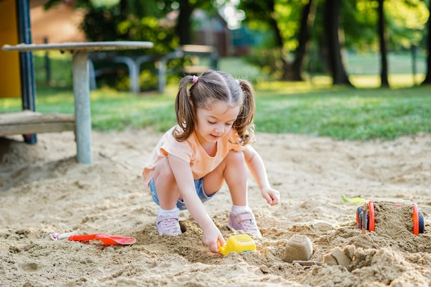 Bellissimo bambino che si diverte in una calda giornata estiva soleggiata Ragazza carina per bambini che gioca nella sabbia nel parco giochi all'aperto