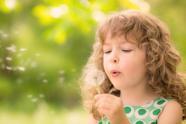 Bellissimo bambino con fiore di tarassaco nel parco primaverile Bambino felice che si diverte all'aperto