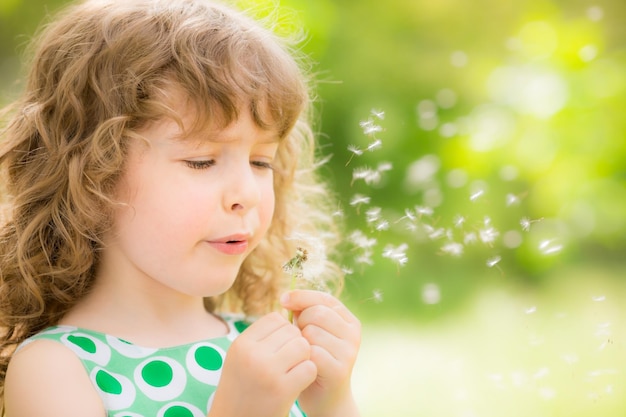 Bellissimo bambino con fiore di tarassaco nel parco primaverile Bambino felice che si diverte all'aperto