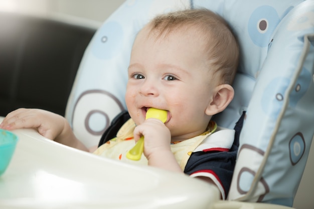 Bellissimo bambino di 9 mesi che gioca con il cucchiaio mentre mangia