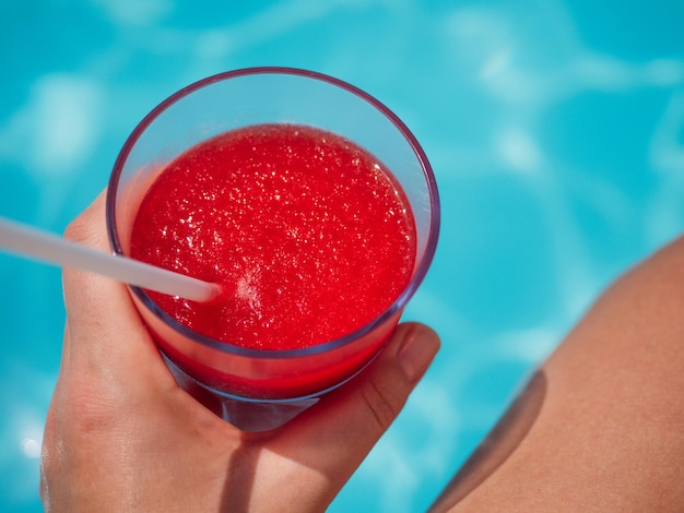 Bellissimo bicchiere con un frullato di fragole rinfrescante e una bella donna sullo sfondo della piscina Vista dall'alto primo piano Concetto di vacanza e viaggio Momenti di festa