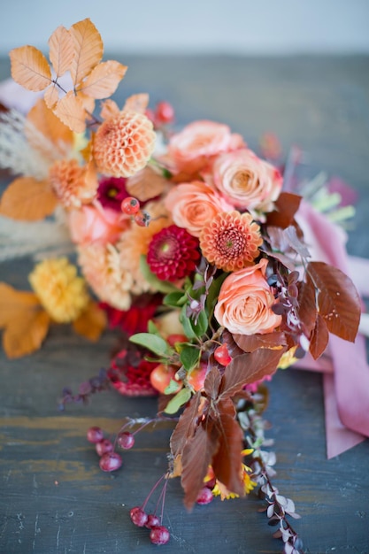 Bellissimo bouquet autunnale con fiori e bacche arancioni e rossi Bouquet autunnale con nastri su un tavolo di legno