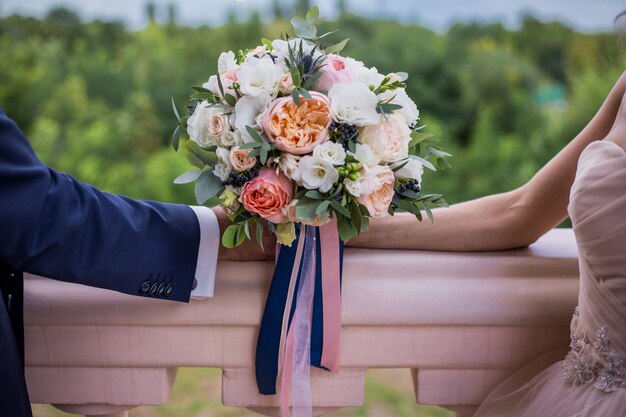 Bellissimo bouquet da sposa di rose e pioni con strisce, tenendo con le mani su sfondo verde. Matrimonio
