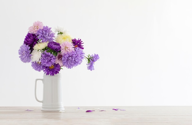 Bellissimo bouquet di astri in brocca bianca su sfondo bianco muro