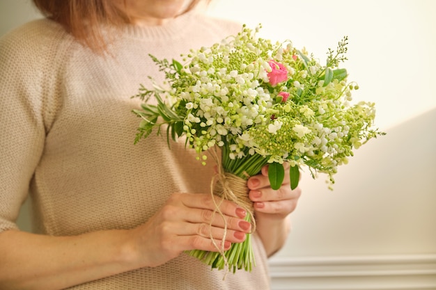 Bellissimo bouquet di fiori di mughetto, rosa rosa, rami verdi in mano donna