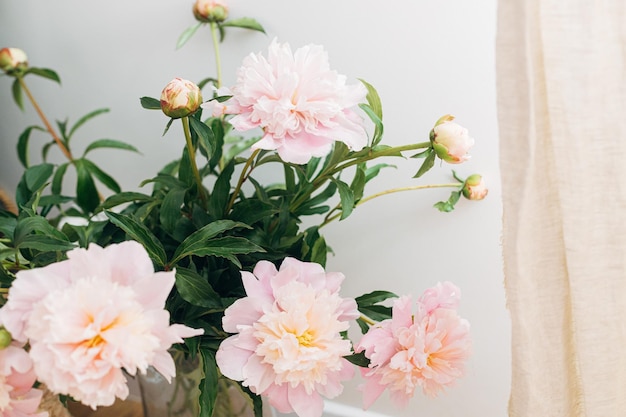 Bellissimo bouquet di peonie nella moderna camera boho Fiori di peonia rosa delicati in vaso su sfondo rustico immagine lunatica Arredamento bohémien moderno dettagli interni comodi ed eleganti