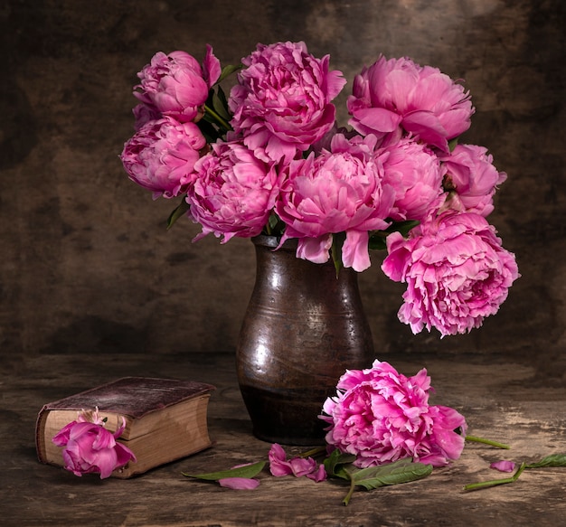 Bellissimo bouquet di peonie rosa in vaso e vecchio libro su un tavolo di legno