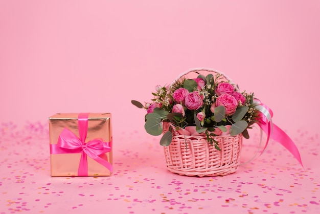 Bellissimo bouquet di rose rosa e rami di eucalipto in un cesto regalo su sfondo rosa con coriandoli e una scatola a sorpresa per un compleanno San Valentino o festa della mamma Vista dall'alto dallo spazio della copia