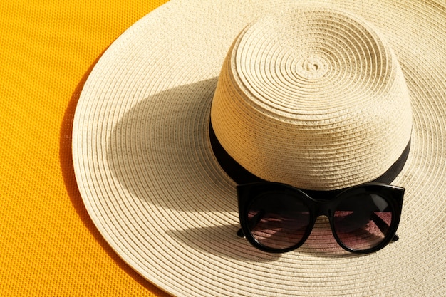 Bellissimo cappello di paglia con occhiali da sole sul colore giallo vivace sfondo vivo. Vista dall'alto.
