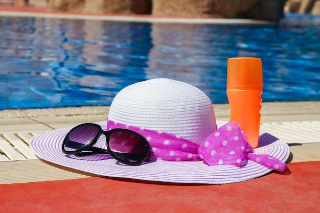 Bellissimo cappello vicino alla piscina con sfondo crema e occhiali