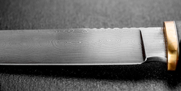 Bellissimo coltello da caccia fatto a mano con una lama grigia affilata su uno sfondo di cemento scuro