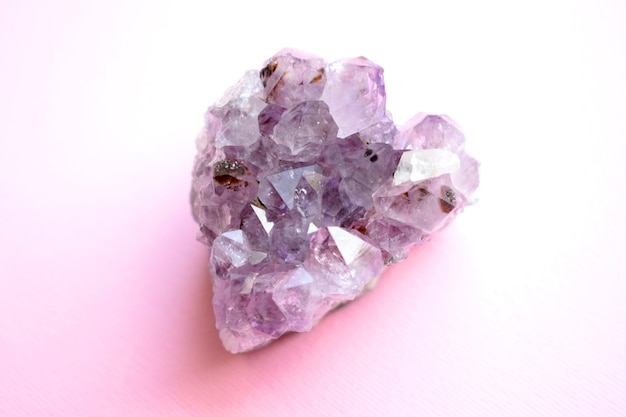 Bellissimo druse di ametista minerale viola naturale a forma di cuore su sfondo rosa. Grandi cristalli di una gemma.