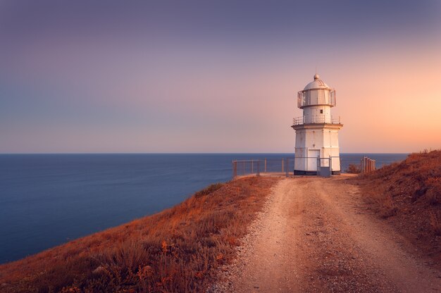 Bellissimo faro bianco sulla costa dell'oceano al tramonto