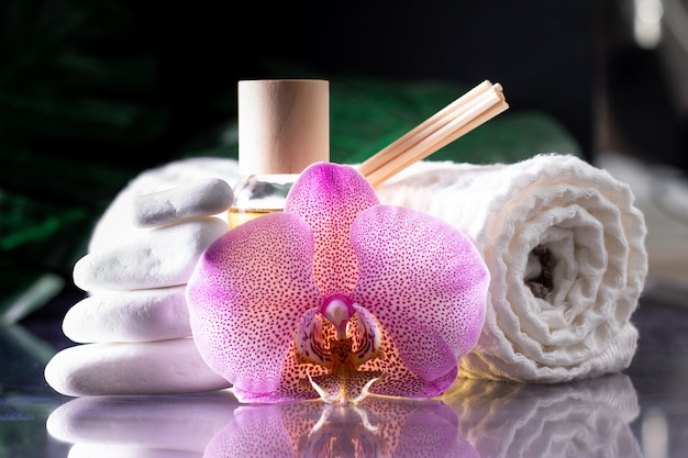 Bellissimo fiore di orchidea lilla, bottiglia trasparente di olio o profumo giallo, bastoncini di legno e asciugamano arrotolato