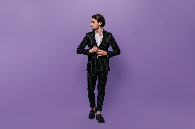 Bellissimo giovane gentiluomo in abito elegante, camicia bianca e scarpe nere, raddrizzando la giacca e guardando da parte