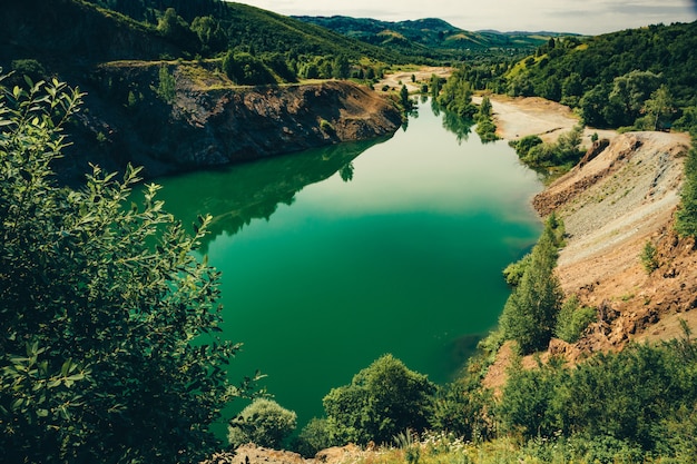 Bellissimo lago verde di forma allungata con costa rocciosa di pietrisco circondato da vegetazione. Cava profonda allagata per l'estrazione di minerali.