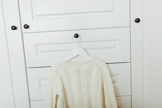 Bellissimo maglione invernale per ragazze sul gancio sullo sfondo del guardaroba bianco