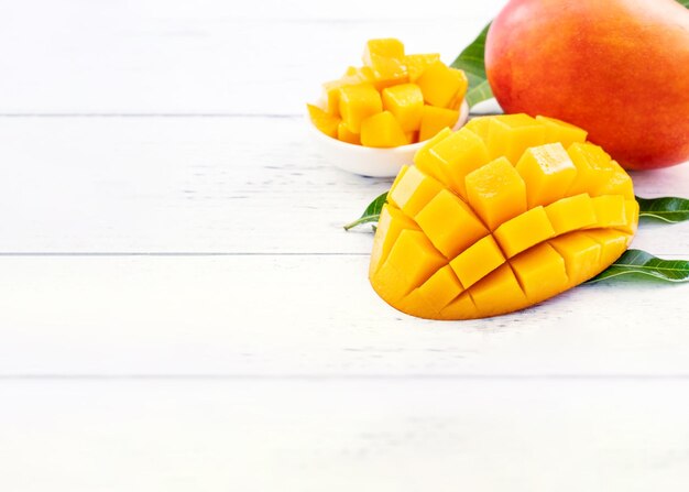 Bellissimo mango tritato con foglie verdi su sfondo di legno di colore bianco brillante Sopra la vista dall'alto spazio piatto per la copia primo piano Concetto di frutta tropicale