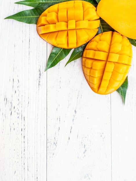 Bellissimo mango tritato con foglie verdi su sfondo di legno di colore bianco brillante Sopra la vista dall'alto spazio piatto per la copia primo piano Concetto di frutta tropicale