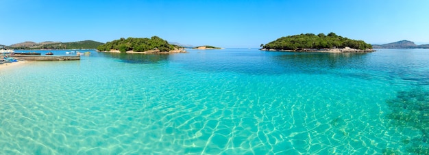 Bellissimo Mar Ionio con acque turchesi limpide e vista sulla costa estiva mattutina dalla spiaggia (Ksamil, Albania). Panorama di punti tre scatti.