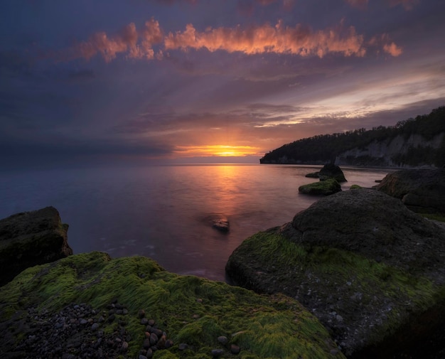 Bellissimo mare in autunno con tramonto epico con massi di alghe verdi.