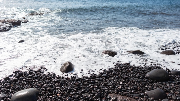 Bellissimo oceano con onde schiumose e spiaggia di pietra nera Spiaggia sull'isola vulcanica di Madeira